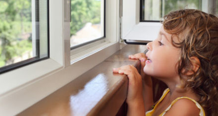 Mädchen schaut am Tag beim richtigen Lüften aus dem Wohnzimmer-Fenster