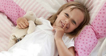 Fröhliches Mädchen im gesunden Kinderbett mit Kuscheltier im Arm