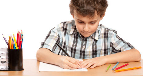 Schreibendes Kind (Junge) an mitwachsendem Schreibtisch mit Stiften