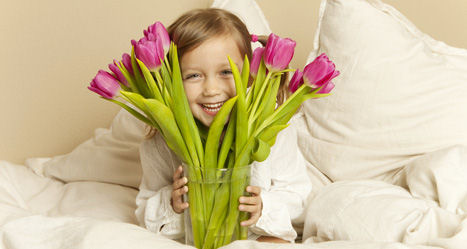 Strahlendes Mädchen im Schlafzimmer schaut zwischen Strauß aus Tulpen hindurch