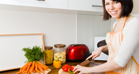 Frau an Arbeitsplatte schneidet Gemüse, freut sich über Ergonomie in der Küche